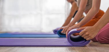 Hareketli yoga minderlerini saran ellerin yakın çekimi, güneşli bir stüdyoda tatmin edici bir seansın sonunu işaret ediyor.