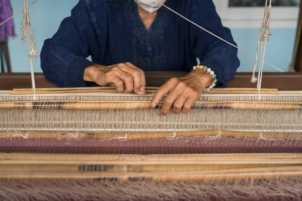 A detailed view of an artisan\'s hands meticulously weaving Thai silk on a traditional loom, showcasing a timeless craft
