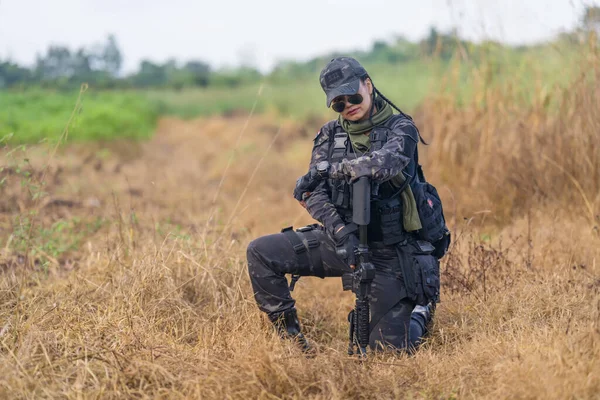 A portrait of a focused Thai female soldier, fully geared during a military training exercise in the field