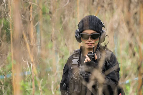 A female Thai soldier in camouflage engages her walkie-talkie for tactical communication amidst field training