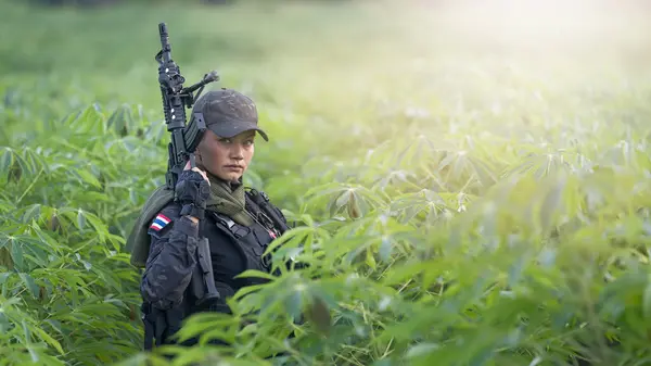 A vigilant female Thai soldier in full gear scans the surroundings during a tactical field training exercise