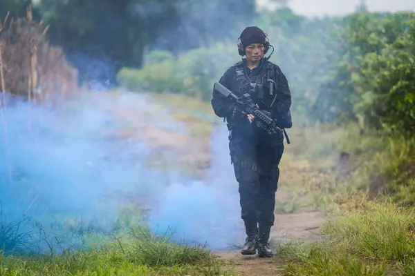 A Thai female soldier presses forward with determination amidst the haze of a smoke bomb in a rigorous field training exercise