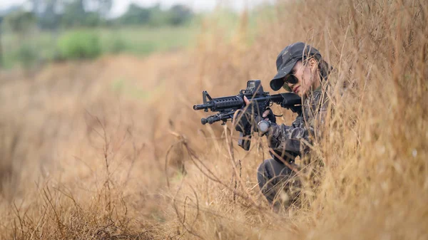 A portrait of a focused female Thai soldier lying prone, aiming her rifle during a tactical field training session