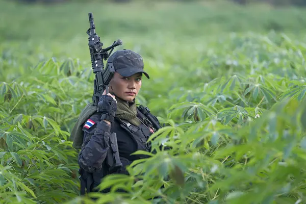 A vigilant female Thai soldier in full gear scans the surroundings during a tactical field training exercise