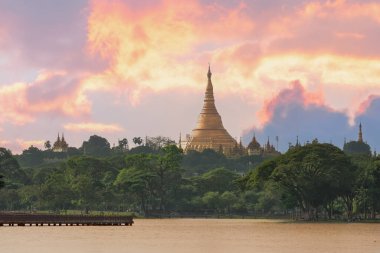 Yangon, Myanmar 'daki ikonik Shwedagon Pagoda Kandawyi Gölü' nün sakin kıyılarından izlenen canlı bir günbatımı gökyüzüne karşı görkemli bir şekilde ayakta duruyor.