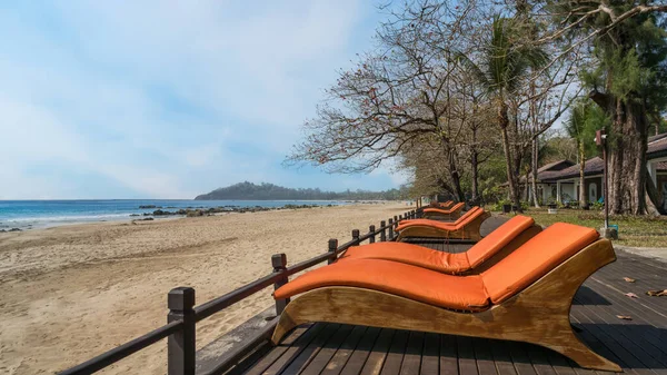 A serene view of Ngapali Beach in Myanmar showcasing sun loungers awaiting visitors, the gentle sea breeze rustling through trees, and a clear horizon beyond