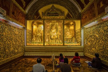 Mandalay, Myanmar, 5 Aralık 2023: Shwe Kyi Myin Paya tapınağındaki üç altın Buda heykeli yerel Myanmar Budist dualarıyla meditasyon yapıyor.