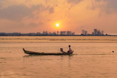 Pyay, Myanmar, 3 Mart 2023: balıkçı Irrawaddy Nehri 'nin sakin sularında gün batımında canlı bir günbatımı gökyüzünün altında geziniyor, Pyay, Myanmar' ın dingin balık tutma geleneklerini somutlaştırıyor.