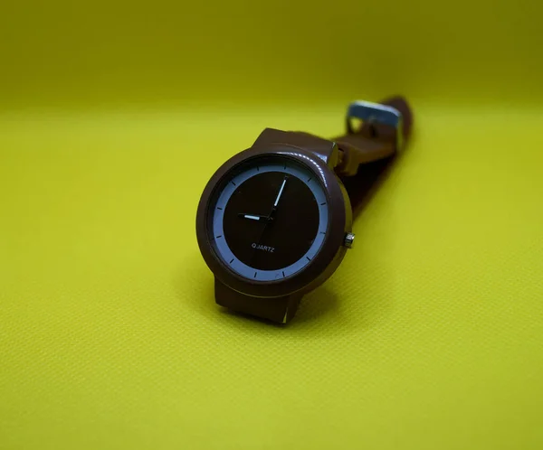 黄色の背景に茶色の腕時計 — ストック写真