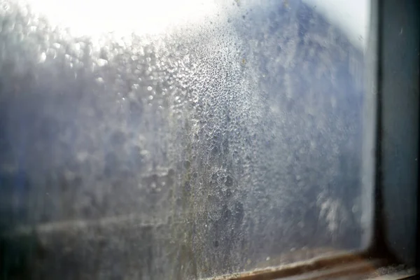 Dirty window glass with dust and dried raindrops backlit with a sunlight on a blurred background