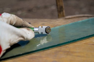 Deri eldivenli insan eli bir cam kesici tutar.