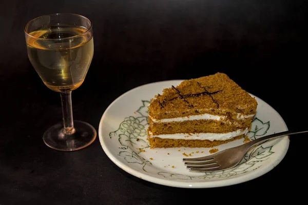 A piece of layer cake and glass of white wine on dark background