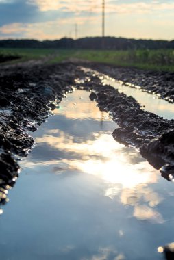 Toprak yol birikintisinde bulutlu gökyüzünün yansıması