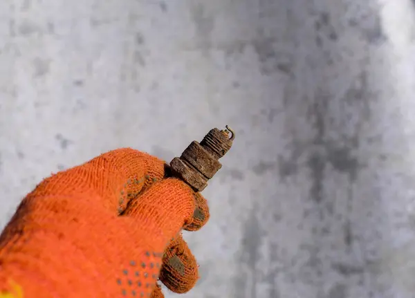 stock image A hand in an orange glove holds a rusty spark plug