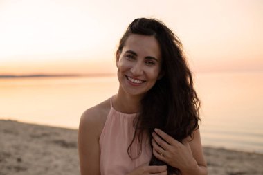 Neşeli güzel bir kadın gülümsüyor ve pembe günbatımı gökyüzünün arka planında poz veriyor