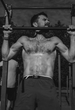 Genç bir sporcu açık hava spor alanında barfiks çekiyor.