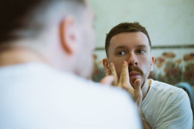 Aynanın yanındaki adam yüzüne masaj yapıyor.