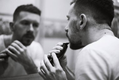 Bir adam aynanın önünde tıraş olur.