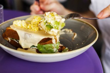 Adam peynirli tost ve çırpılmış yumurta yiyor.