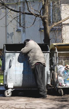 Evsiz bir adam çöp tenekesinde yiyecek arıyor.