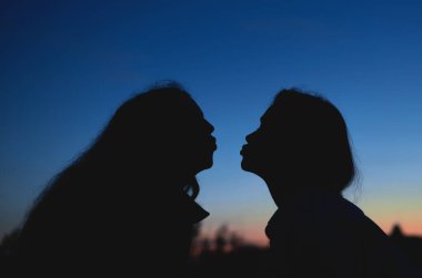 Güneş altında öpüşen iki lezbiyen kadının yakın portresi.