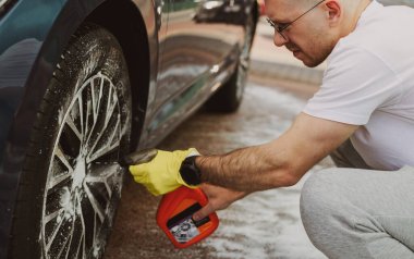 Bir adam araba tekerleklerini köpükle temizler.