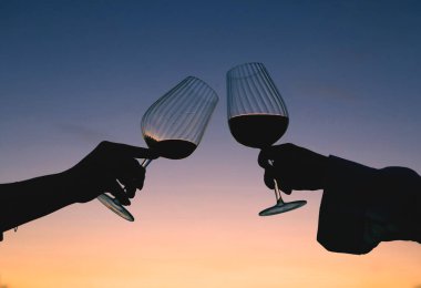 Bir kadının elinde gün batımına karşı bir kadeh şarap.