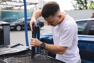 Adam araba paspaslarını süpürüyor.