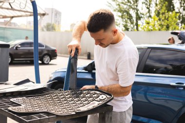 Adam araba paspaslarını süpürüyor.