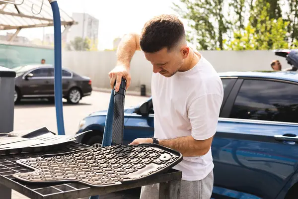 Adam araba paspaslarını süpürüyor.