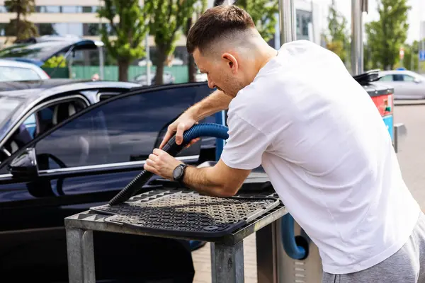 Adam araba paspaslarını süpürüyor.