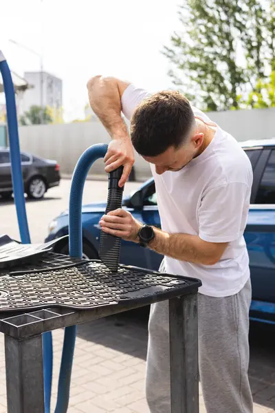 Adam araba paspaslarını süpürüyor.