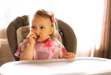 Küçük kız yüksek sandalyede otururken yemek yiyor.