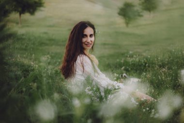 Güzel bir yaz portresi, beyaz bir elbise içinde çimlerin üzerinde oturmuş ve doğanın tadını çıkarıyordu.