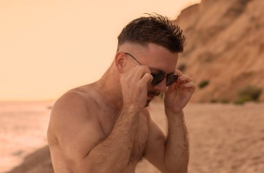 Kumsalda güneş gözlüklü yakışıklı bir adam.