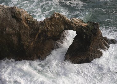 Dalgalar, Point Reyes Ulusal Deniz Kıyısı 'ndaki bir kaya kemerinde koşuşturuyor.
