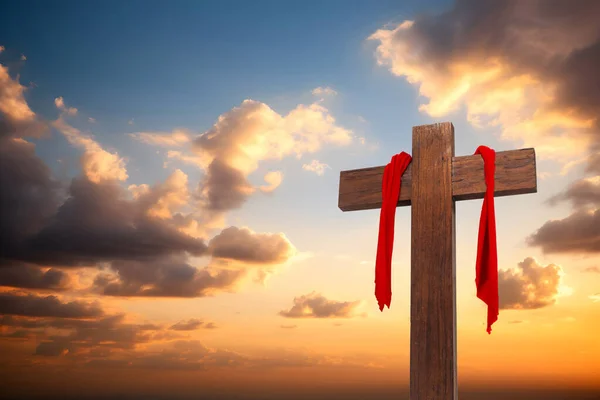 Wooden cross with red cloth wrapped around on sunset sky background, crucifix and resurrection of Jesus