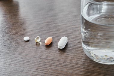 Kahverengi bir masanın üzerinde bir bardak suyla çeşitli haplar, reçeteye göre önceki diyet. Semptomatik tedavi. Mevsimsel terapi gribi.