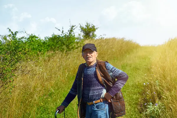 Bıyıklı ve gözlüklü gülümseyen yaşlı adam çimenli bir yolda duruyor, baston tutuyor ve kolsuz koyun derisi ceket giyiyor. Dedemin portresi güneşli bir zemine kurulmuş ve kameraya bakıyor..
