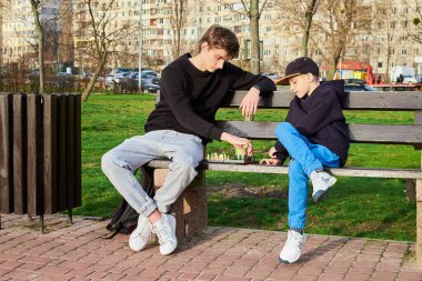 Ergen ve 8 yaşında bir çocuk parkta bankta oturmuş satranç oynuyorlar. Genç, küçük erkek kardeşine nasıl oynanacağını öğretiyor. İkisi de oyuna odaklanmış ve birbirlerine eşlik etmekten zevk alıyorlar..