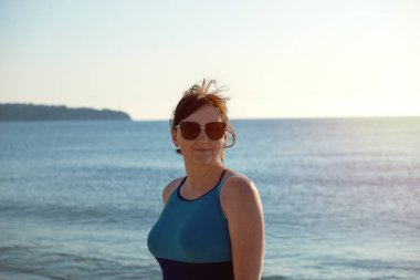 Kendinden emin, olgun bir kadın plajda kapalı bir mayo ve güneş gözlüğü takarak gün geçirmekten zevk alır..
