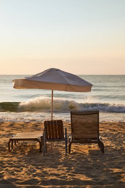 Gün batımında iki sandalye ve bir şemsiyeyle plaj kaçamağı. Yaz posteri.