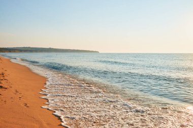 Kumdaki Ayak İzleriyle Huzur Denizi. Bu sakin sahil sahnesinde, yumuşak kumlarda ayak izleri bırakarak kıyıya vuran hafif dalgalar var..