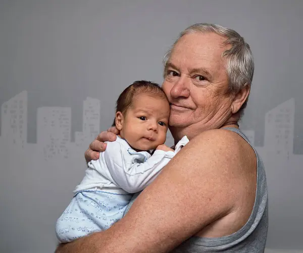 stock image The grandfather gently holds the baby in his arms and hugs him. The grandson continues the family.
