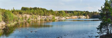 Kayalık uçurumlar ve yoğun yeşil ormanlarla çevrili berrak, berrak bir gökyüzü altında doğa ve açık hava aktiviteleri için mükemmel berrak mavi suların yer aldığı sakin bir göl manzarası..