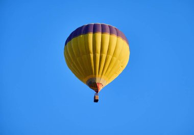 Canlı sarı bir sıcak hava balonu açık mavi gökyüzünde zarifçe süzülür, macera ve özgürlük hissi verir..