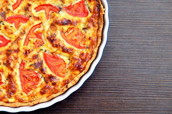 Taze domates dilimleri ve erimiş peynirli nefis ev yapımı kiş, seramik bir tabakta mükemmel pişmiş. Kahvaltı, brunch ya da akşam yemeği için nefis bir turta..