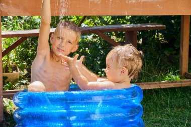 İki genç çocuk, şişme mavi bir havuzda güneşli bir günün tadını çıkarıyorlar. Suyla oynuyorlar ve bahçede eğleniyorlar..