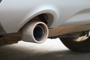 Araba egzoz borusu ve arka lastiğin yakın görüntüsü. Resim, otomotiv bakımı, emisyonlar ve bakım konuları için uygun olan aracın mekanik bileşenlerini vurgular.