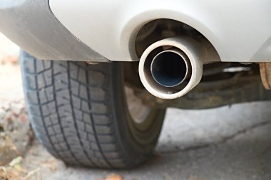 Araba egzoz borusu ve arka lastiğin yakın görüntüsü. Resim, otomotiv bakımı, emisyonlar ve bakım konuları için uygun olan aracın mekanik bileşenlerini vurgular.